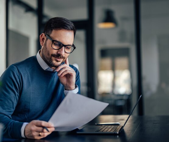 Mann hält Rechnung in der Hand uns liest | © iStock/nortonrsx