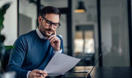 Mann hält Rechnung in der Hand uns liest | © iStock.com/nortonrsx