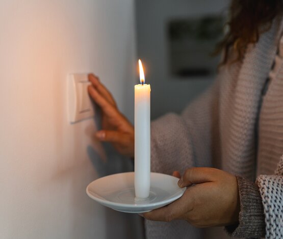 Hand hält Kerze in dunklem Raum bei Stromausfall | © iStock.com/stefanamer