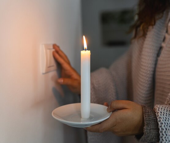 Hand in völliger Dunkelheit mit einer Kerze, die versucht, das Licht während eines Stromausfalls einzuschalten