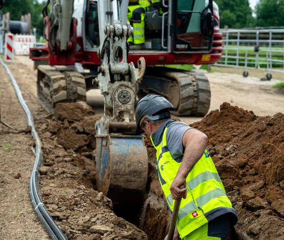 Bagger zieht einen Graben für das Erdkabel, ein Mitarbeiter steht mit einer Spate im Graben